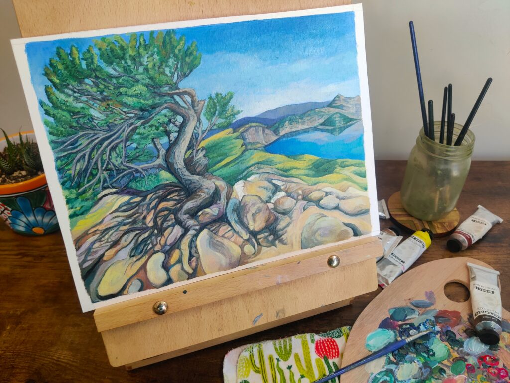 Painting of a gnarled whitebark pine tree on the summit of Mount Scott, with Crater Lake and Wizard Island in the background, shown on easel